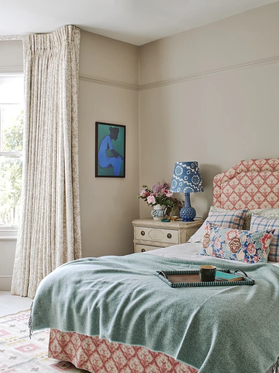 Dormitorio con muros color griege. Cama de dos plazas con textiles color menta, cojines estampados y cabecero de tela color naranjo y rosa claro.