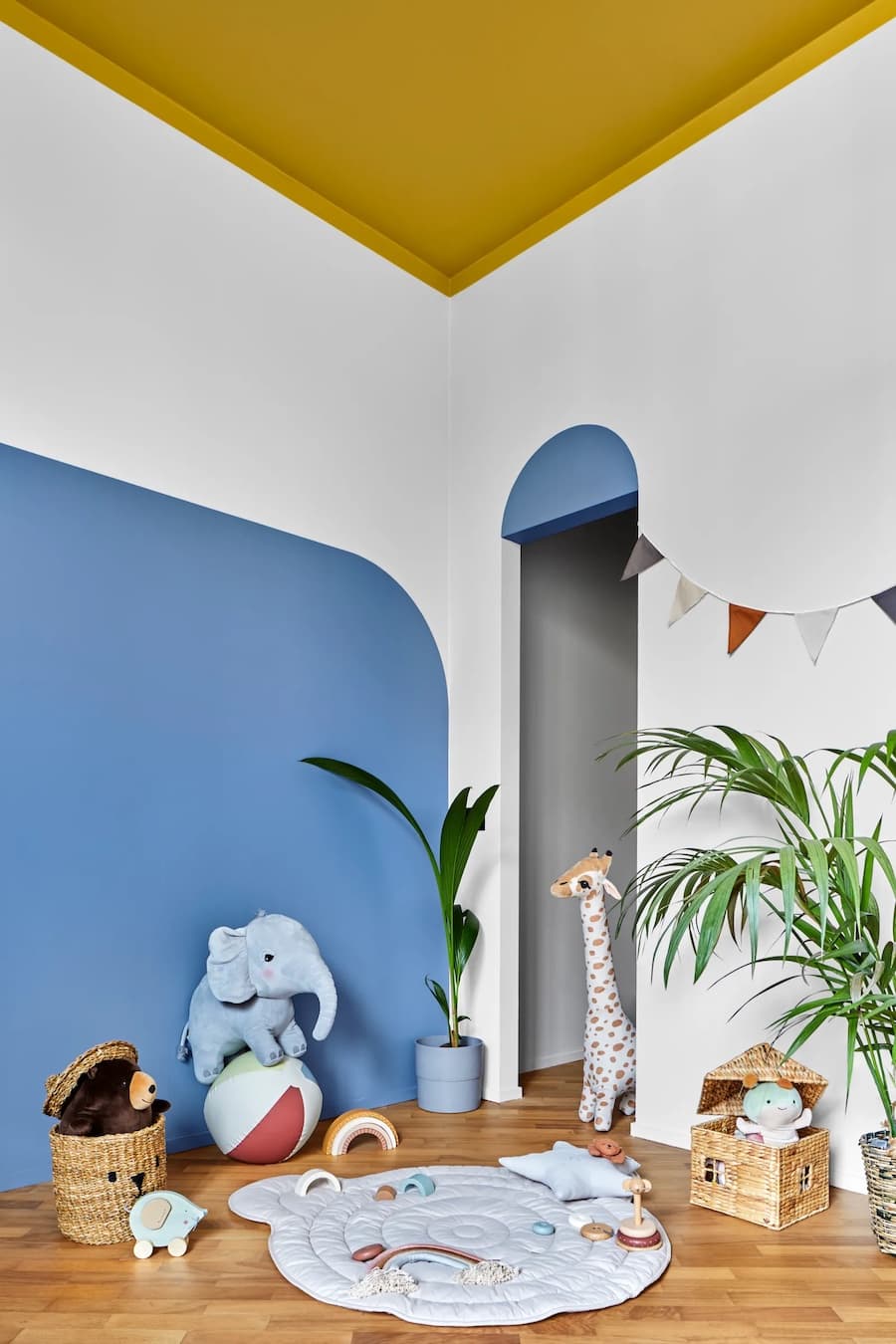 Dormitorio infantil con techo y piso pintado amarillo. Muro azul, animales de peluche y plantas