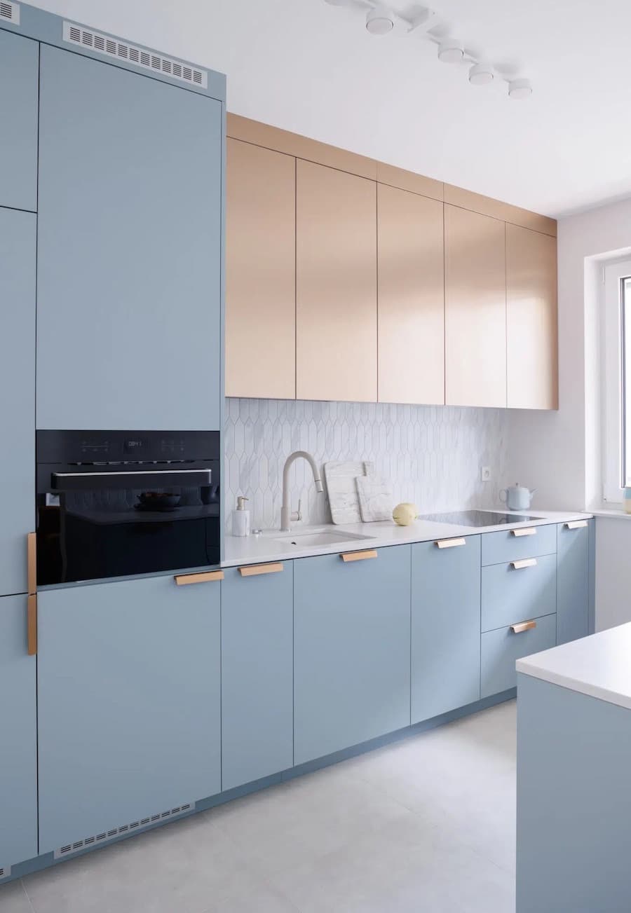 Cocina alargada con muebles de color azul bruma y algunos muebles superiores de madera clara.