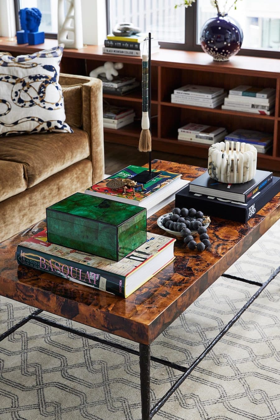 Mesa de centro de madera con un gran libro y una caja verde. Hay otros libros ordenados y sobre ellos hay más adornos como velas.