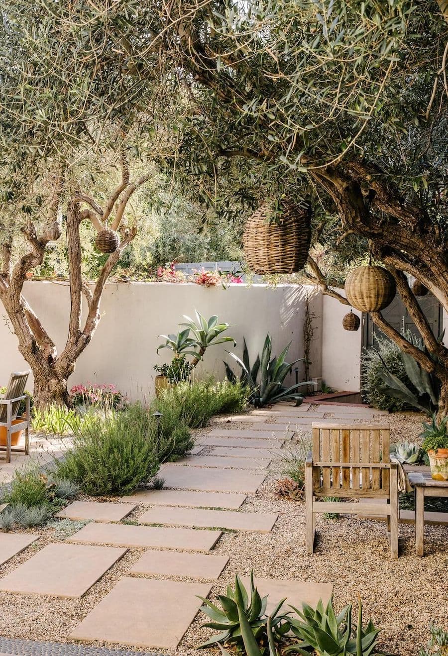 Jardín seco con pastelones y un juego de terraza de madera. De lo árboles cuelgan pantallas de fibras naturales para adornar